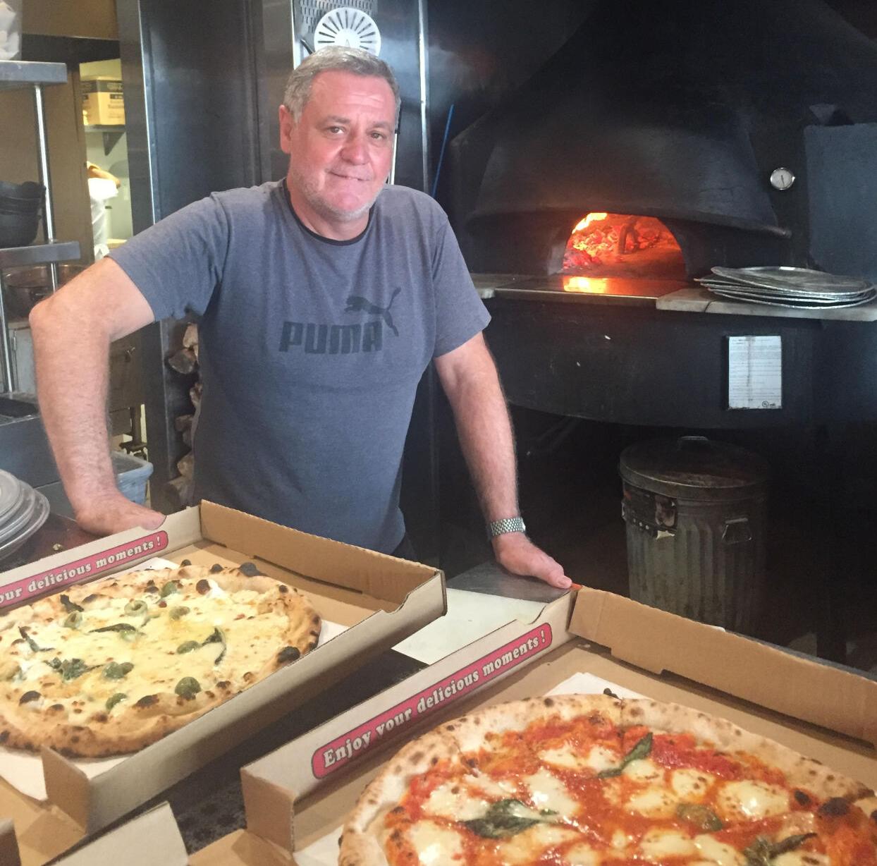 Claudio Blotta in front of All'Acqua's firewood pizza oven